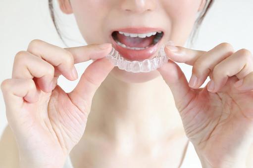 Close-up of a person holding a clear dental aligner against their open mouth, showing how it fits over the teeth.