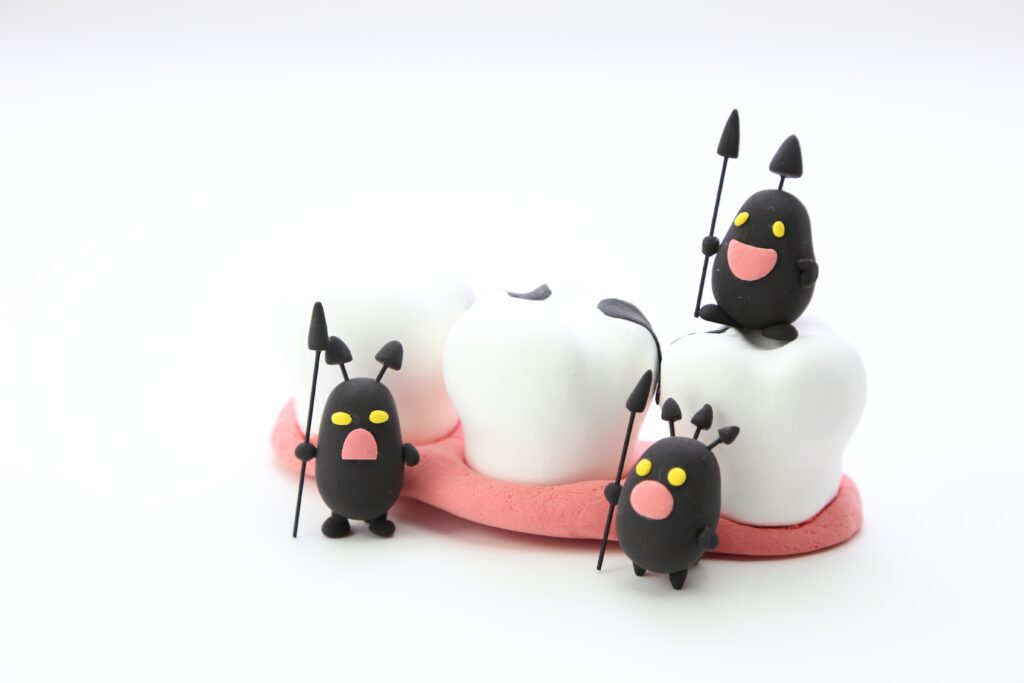 Several small black fondant creatures with yellow eyes and pink mouths stand on a white-and-pink fondant cake, each holding thin skewers with tiny black cone shapes on top, set against a white background.