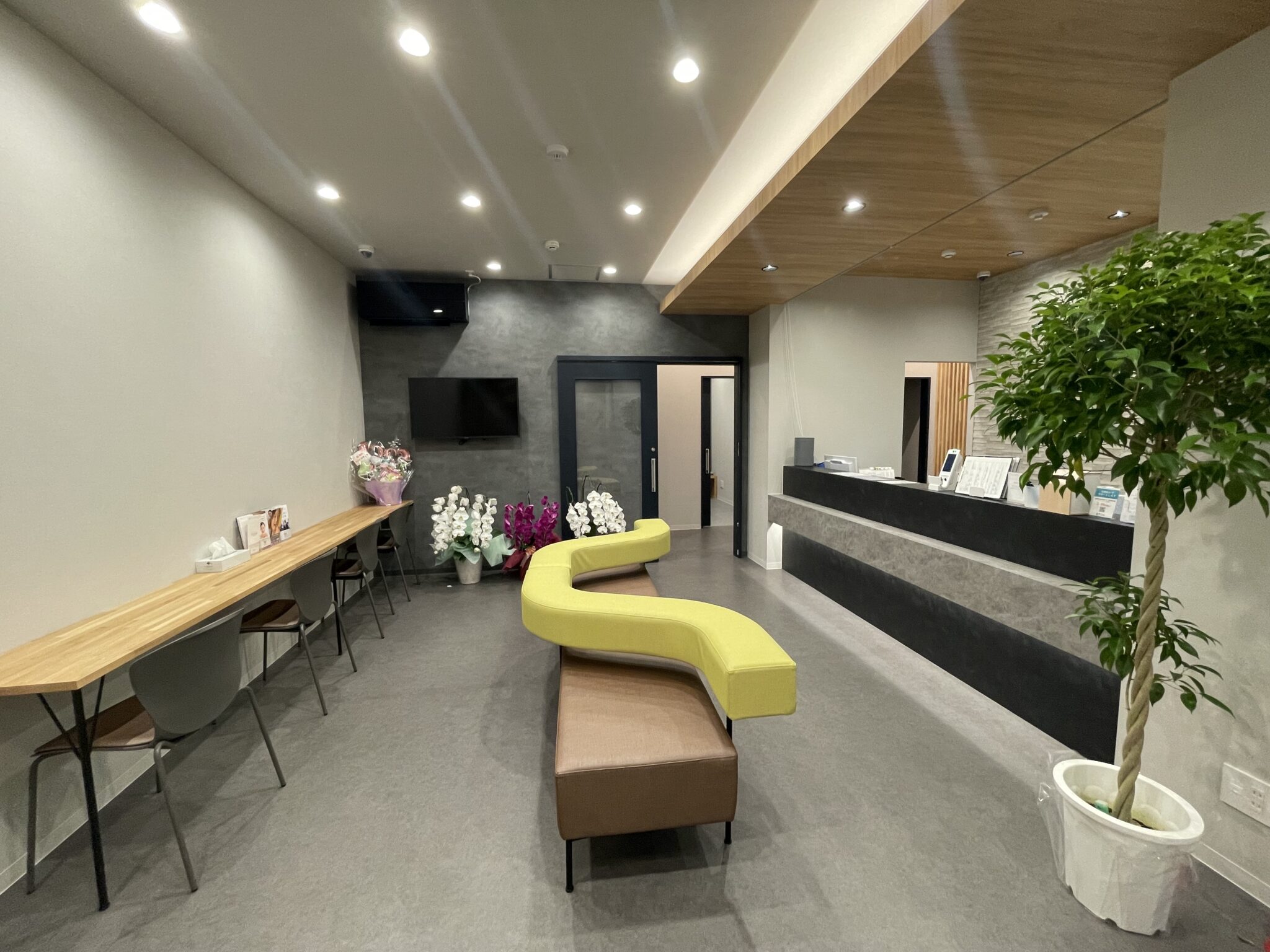Modern lobby interior with a long wooden counter and black chairs on the left, yellow curved seating in the center, and a reception desk to the right.